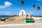 A man in an orange t-shirt is looking at the Church fortress of San Antonio on Mozambique island, with three palm trees on sand.