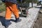 Man in orange uniform using vibrational paving stone machine for finish on a sidewalk road construction site.