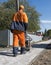 Man in orange uniform using vibrational paving stone machine for finish on a sidewalk road construction site.