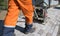 Man in orange uniform using vibrational paving stone machine for finish on a sidewalk road construction site.