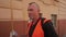 A man in an orange vest and gloves speaks on the move on a city street.