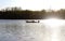 Man out in fishing boat on river in early foggy morning with smoke from outboard motor showing against trees