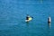 A man in a paddle boat rowing across the vast deep blue ocean water in the harbor surrounded buoys in the water at Baby Beach