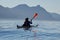 Man paddles sea kayak on calm summer morning on adventure near northwestern Vancouver Island with blue mountains, ocean and sky