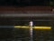 Man is paddling in a yellow kayak on a tranquil body of water.