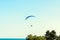 Man paragliding with blue parachute above water sea, clear sky