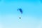 Man paragliding with blue parachute above water sea, clear sky