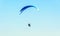 Man paragliding with blue parachute above water sea, clear sky