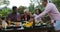 Man Passing Food To People Sitting At Table Eating Young Friends Group Gathering On Summer Terrace