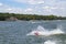 Man on Personal Water Craft landing in a spray of water after jumping a wake at the lake with speedboat and houses and boat docks