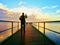 Man photograph morning sea from long wooden mole in wharf.