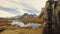 Man photographer hiker shoot photo near lake to snowy mounts.Behind view. Sunny autumn day Hiking in colorful red forest