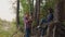 Man photographing woman by mobile phone in coniferous forest. Happy woman posing on tree roots in pine forest for mobile