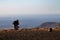 A man photographs an island in the ocean, squatting on the edge of a cliff