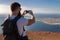 The man photographs an island in the ocean, standing on the edge of a cliff