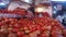 Man picking tomatoes from a large pile at market stand and weighing them.