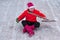 Man in a pink Christmas hat and winter boots in an red sweater is sitting in a lotus position on the site of his yard with a