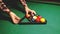 A man in a plaid shirt and a fashionable wristwatch puts the position to the game of Billiards Pool. Dim lights