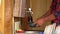 Man in a plaid shirt washes a blue metallic bowl in the kitchen sink of a country house.