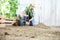 Man plant out a seedling in the vegetable garden, work the soil with the garden spade, near wooden boxes full of plants