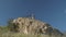 A man plays the Australian Aboriginal musical instrument Didgeridoo on a rock ledge against a blue sky. View from bottom