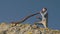 A man plays the Australian Aboriginal musical instrument Didgeridoo on a rock ledge against a blue sky. View from bottom