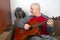 Man plays the classical guitar next to a gray cat on a white background