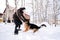 A man plays fetch with a dog in the snowy yard of a house.