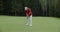 A man plays golf, hitting a golf ball with a club and pushes it into the hole