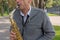 Man plays on saxophone in the park. Street musician with sax performs music for charity. Public solo performance by wind