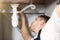 Man plumber in uniform fixing the sink pipe with adjustable spanner in his hand lying on the kitchen floor professional plumbing