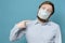 Man points index finger to the medical mask on his face, which is not snug due to the shaggy beard. Quarantine concept.