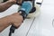 A man polishing the surface of the door of a white sedan with an electric buffing machine. At an auto detailing shop