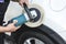 A man polishing the surface of a white sedan with an electric buffing machine. At an auto detailing shop