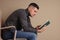 Man with poor posture reading book while sitting on chair against beige background