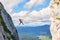 Man posing on Donnerkogel Intersport via ferrata klettersteig ladder, with his leg  hanging out, on a bright sunny day