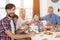 A man is posing and looking at the camera on the background of a family that sits at a festive table for Thanksgiving