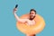 Man posing with orange rubber ring and holding mobile phone, making selfie.