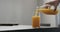Man pour orange juice from glass bottle into highball glass on concrete countertop with copy space