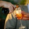 Man is pouring champagne from the bottle in the glass of another man. Evening light. Hand shot, Square image.