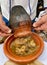 Man pouring Tangia, Tanjia, roasted lamb cooked in clay pots, into ceramic plate. Marrakech, Morocco.