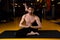 Man practices yoga in a dark gym. He threw his leg behind his head. Shirshasana