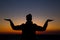 a man practicing yoga on a grassy horizon after sunset. Silhouette against a bright orange sky