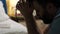 Man is praying. Bearded man sits on floor in bedroom by bed, holds rosary with crucifix in his hands and says prayer