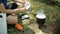 A man preparing a meal in a pot on a gas burner in the forest. Sitting on the ground and stir the soup