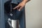 A man presses down on a lever to drop ice cubes from a dispenser into a small stainless bucket. Using a commercial grade hotel ice