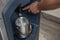 A man presses down on a lever to drop ice cubes from a dispenser into a small stainless bucket. Using a commercial grade hotel ice