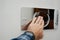 A man is pressing a wall-mounted polished chrome single flush plate to flush the toilet