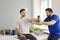 Man professional osteopath chiropractor examining man holding dumbbell in hand in hospital office.