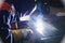 Man in protective attire is welding metal at a workplace in factory.